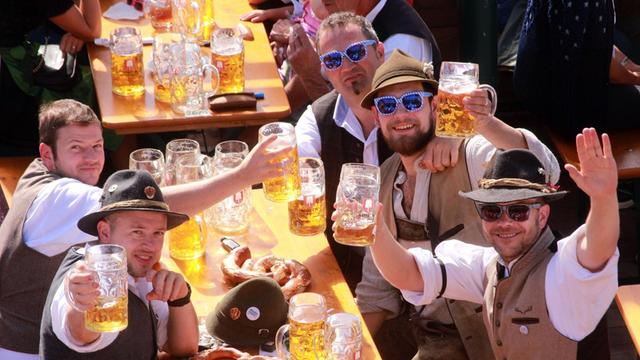 Oktoberfest in München: gut gelaunte Männer aus Niederbayern winken und halten ihre Maßkrüge hoch im Biergarten eines Festzeltes