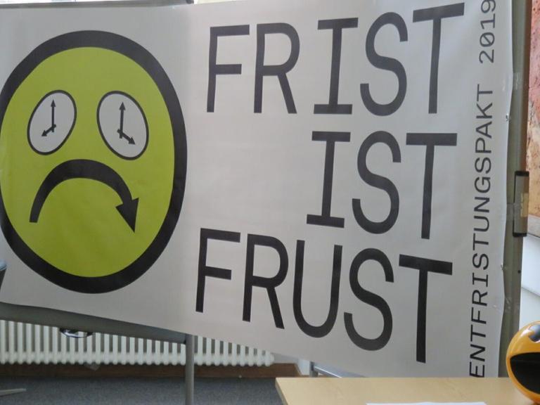 Ein trauriger Smiley mit Augen aus tickenden Uhren. Daneben steht der Schriftzug "Frist ist Frust"