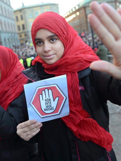 Eine Frau mit einem roten Kopftuch hält ein Schild mit der Aufschrift "Rör inte min Moské! – Rühr ja nicht meine Moschee an!" in der Hand.