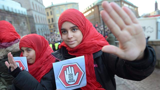 Eine Frau mit einem roten Kopftuch hält ein Schild mit der Aufschrift "Rör inte min Moské! – Rühr ja nicht meine Moschee an!" in der Hand.