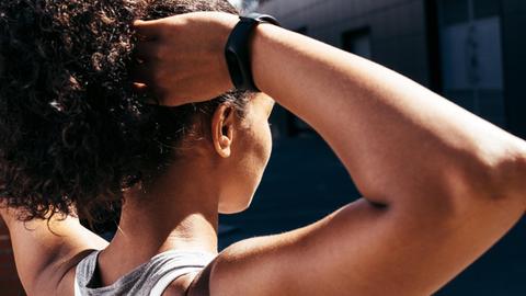 Eine Frau trägt einen Fitness-Tracker am Handgelenk und fährt sich während sie steht durch die Haare.