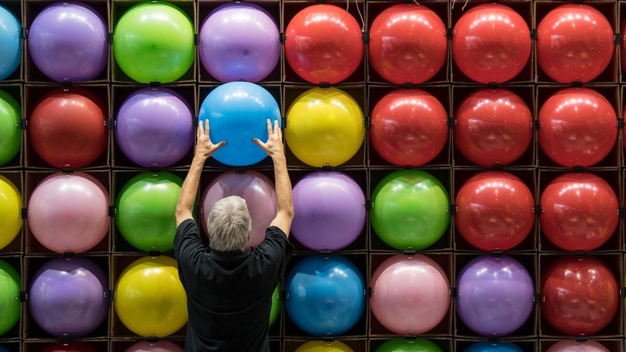 Zur Dekoration eines Standes bringt ein Messebauer zahlreiche bunte Luftballons an eine Wand an. Zur Dekoration eines Standes bringt ein Messebauer zahlreiche bunte Luftballons an eine Wand an.