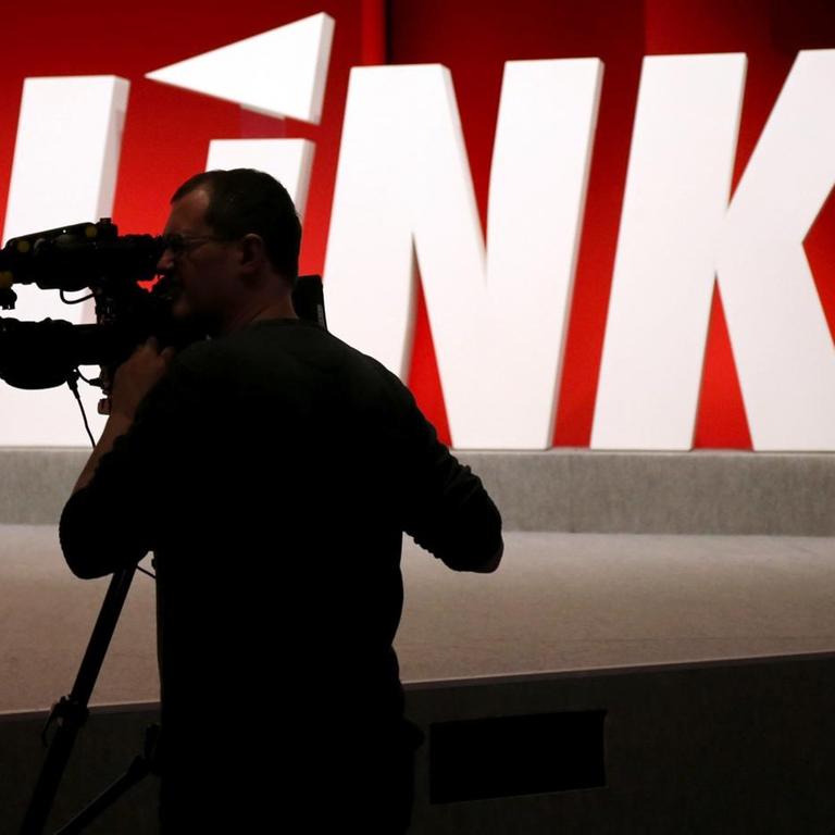 Ein Kameramann steht vor dem Logo der Linkspartei. 