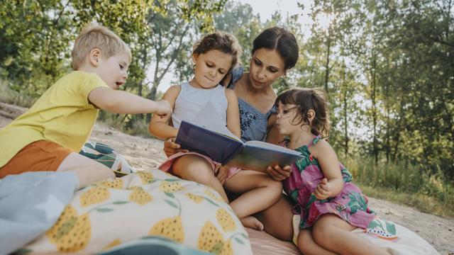 Mature woman and three children reading book at beach model released Symbolfoto MFF06235