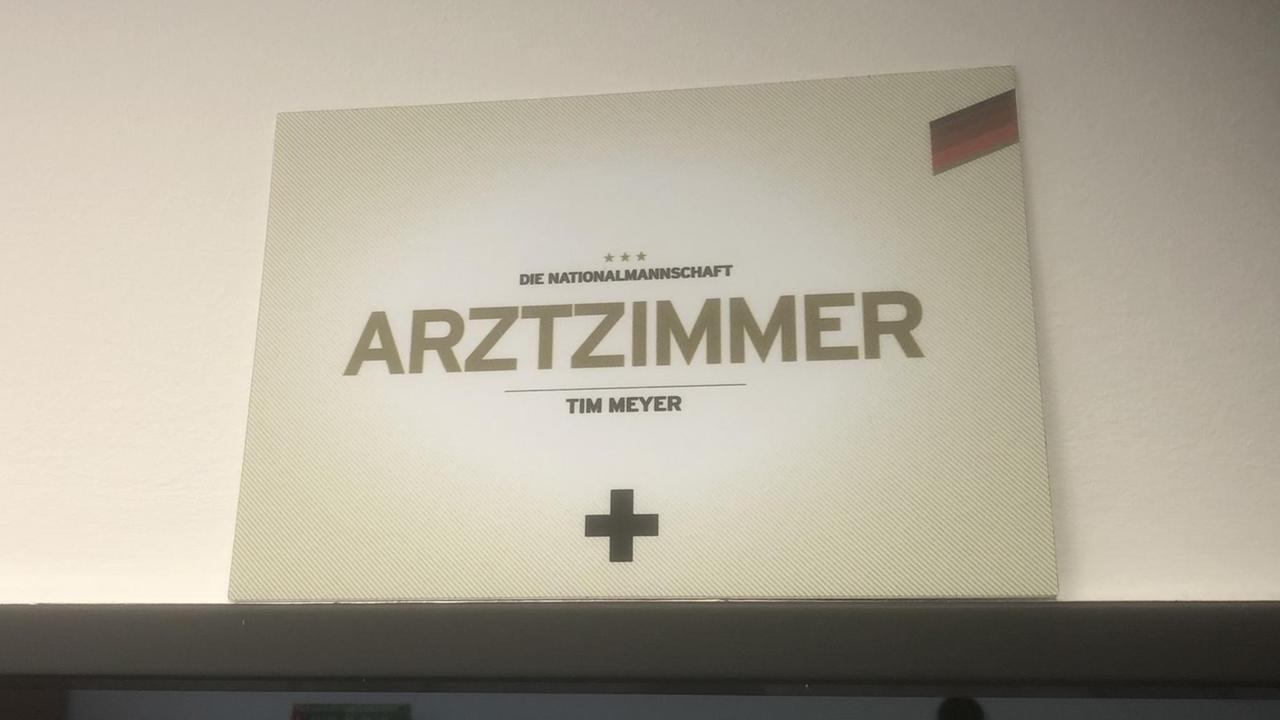Schild mit der Aufschrift: "Arztzimmer". Darüber: "Die Nationalmannschaft". Darunter: "Tim Meyer" Schild mit der Aufschrift: "Arztzimmer". Darüber: "Die Nationalmannschaft". Darunter: "Tim Meyer"