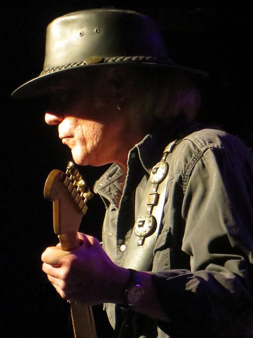 Der Kölner Musiker Klaus "Major" Heuser steht bekleidet mit einem Lederhut auf einer dunklen Bühne und spielt Gitarre.