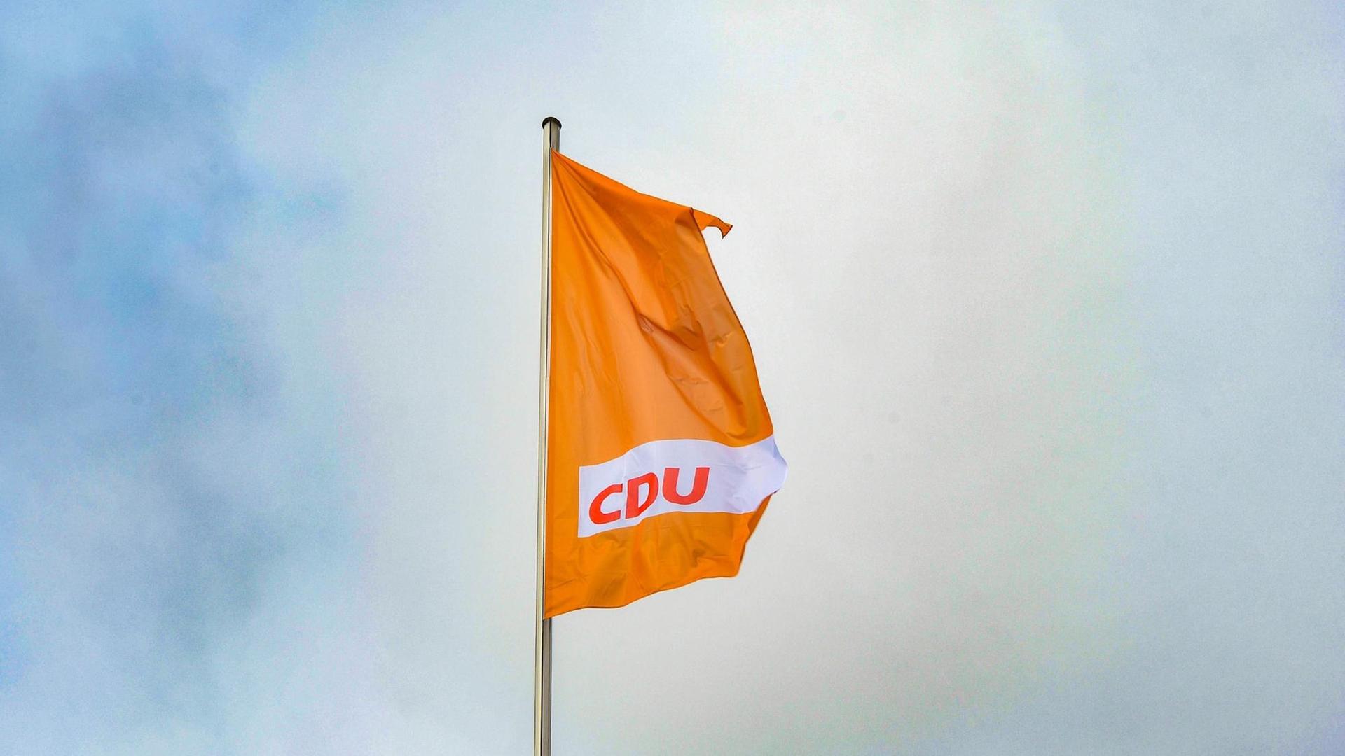Eine orangefarbende Fahne mit dem CDU-Logo weht vor blauem Himmel.