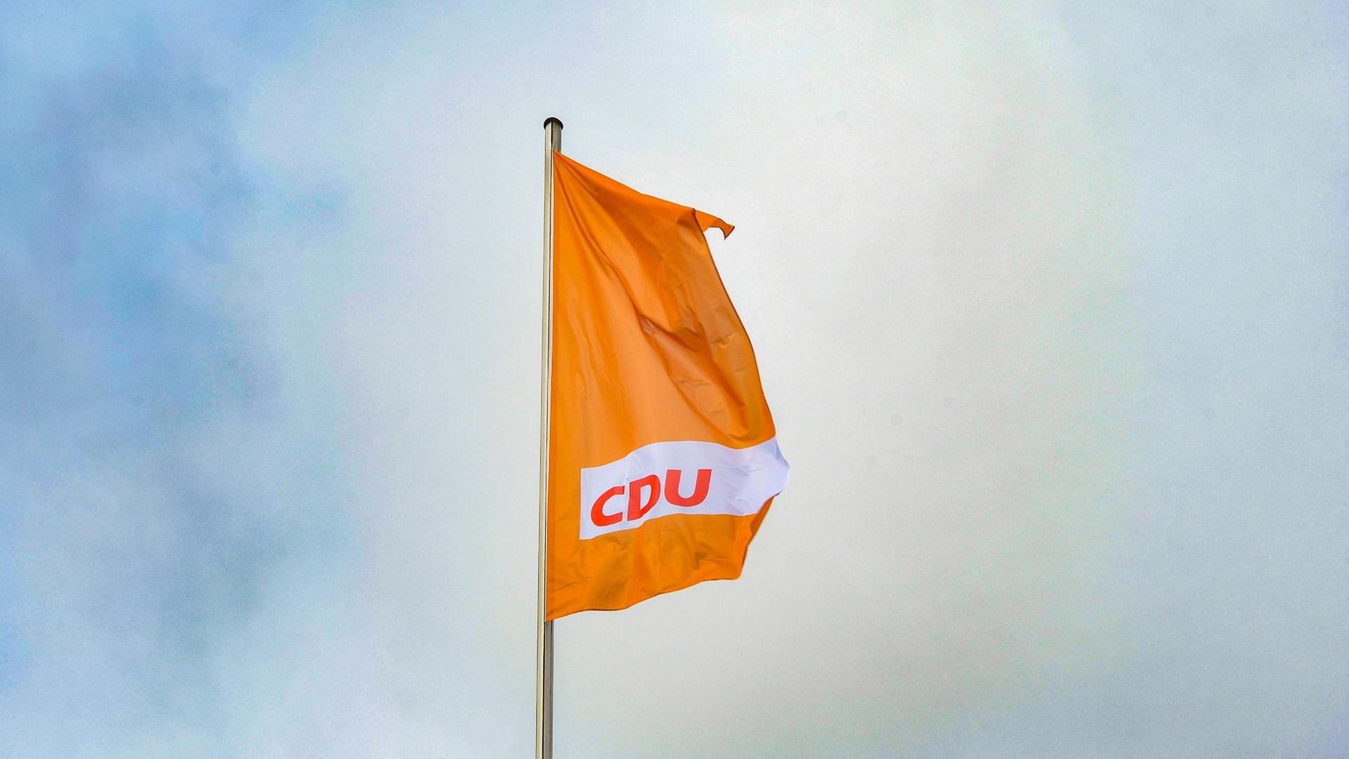 Eine orangefarbende Fahne mit dem CDU-Logo weht vor blauem Himmel. Eine orangefarbende Fahne mit dem CDU-Logo weht vor blauem Himmel.