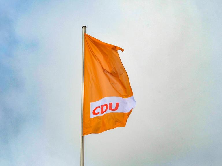 Eine orangefarbende Fahne mit dem CDU-Logo weht vor blauem Himmel.