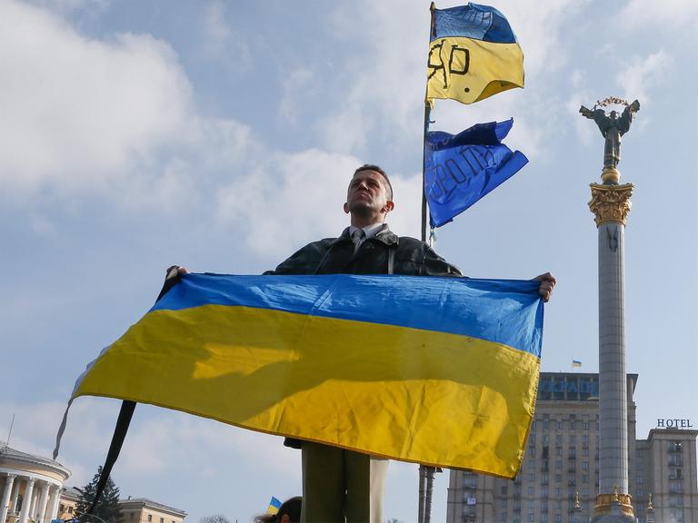 Ein Ukrainer hält in Kiew die Nationalflagge in die Höhe.