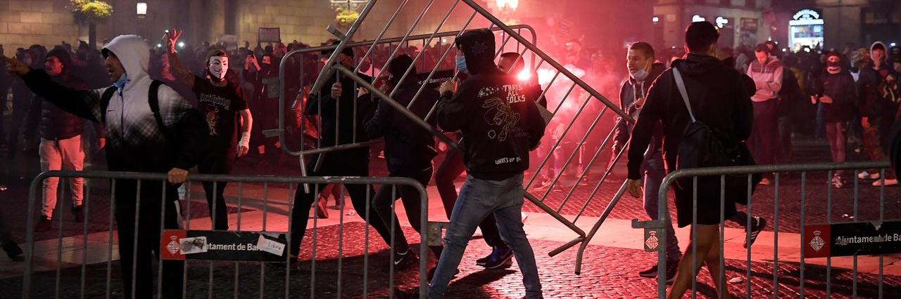 Demonstranten entfernen Absperrgitter der Polizei, im Hintergrund roter Feuerschein
