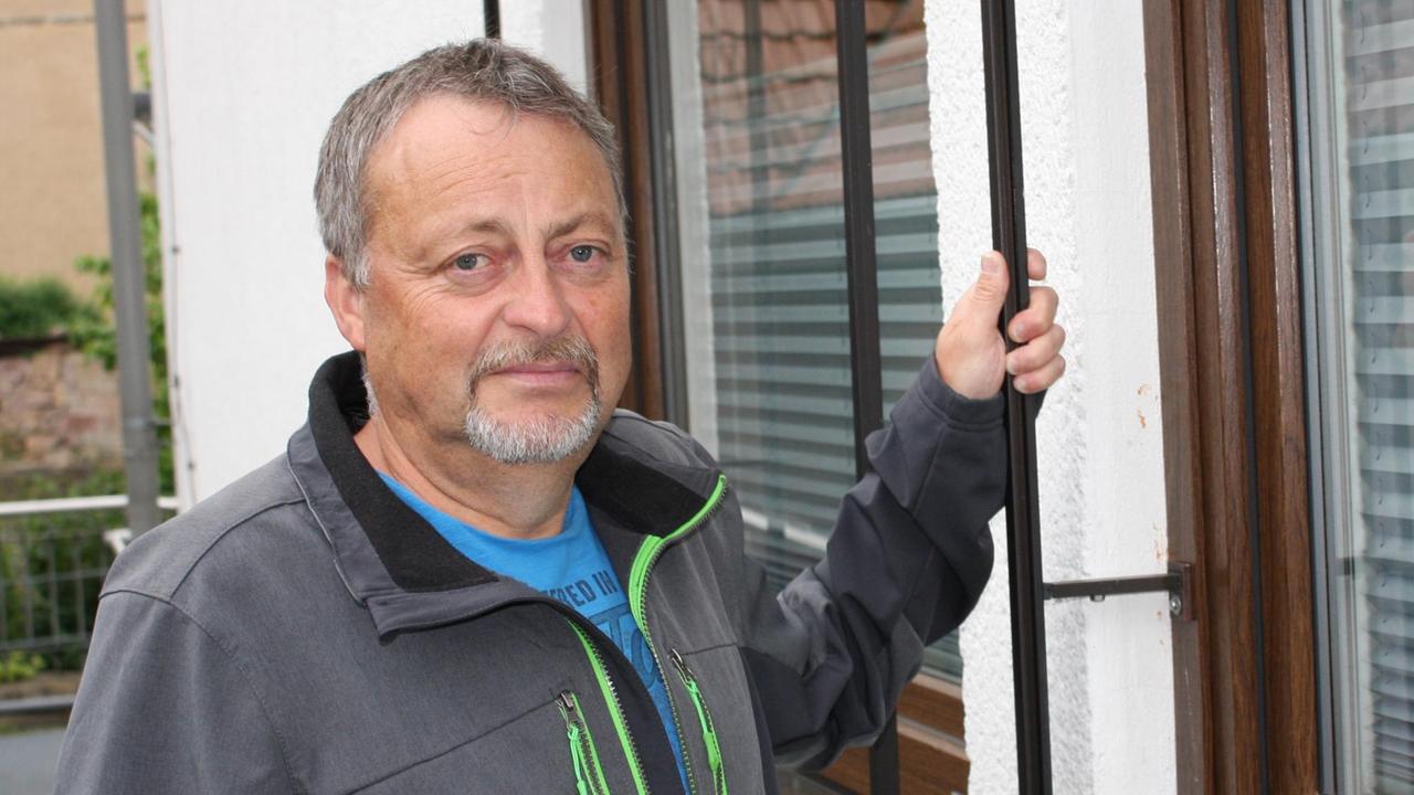 Ein Mann steht außerhalb eines Hauses und blickt ernst in die Kmaera. Ein Mann steht außerhalb eines Hauses und blickt ernst in die Kmaera.