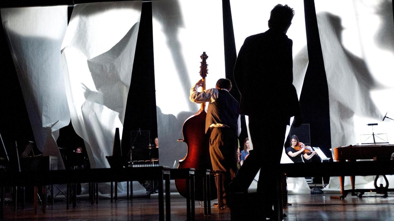 Eine Probenszene des Stückes "Schwarz auf Weiß" von Heiner Goebbels. Auf einer Bühne wehen weiße Tücher, davor spielen mehrere Musiker. Eine Probenszene des Stückes "Schwarz auf Weiß" von Heiner Goebbels. Auf einer Bühne wehen weiße Tücher, davor spielen mehrere Musiker.