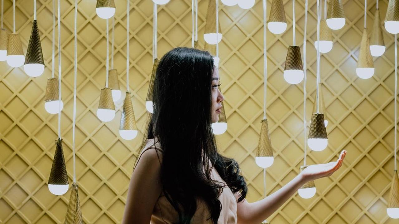 Eine Frau steht vor einer gelben Wand, vor der viele Energiesparlampen hängen. Eine Frau steht vor einer gelben Wand, vor der viele Energiesparlampen hängen.