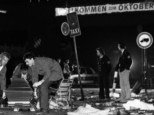 Ein Sarg wird nach dem Bombenanschlag auf dem Münchener Oktoberfest am 26.09.1980 vom verwüsteten Tatort weggetragen. Die Bombe befand sich vermutlich in dem Papierkorb an einem Verkehrsschild rechts im Hintergrund.