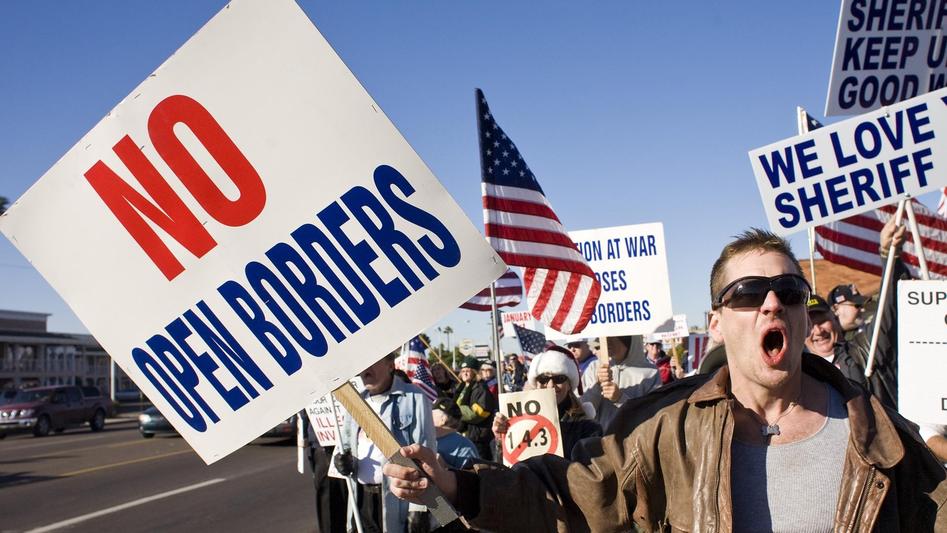 Demonstration in Phoenix gegen Immigration in die USA. "No open borders" steht auf einem Protestplakat, amerikanische Flaggen werden geschwungen. Demonstration in Phoenix gegen Immigration in die USA. "No open borders" steht auf einem Protestplakat, amerikanische Flaggen werden geschwungen.