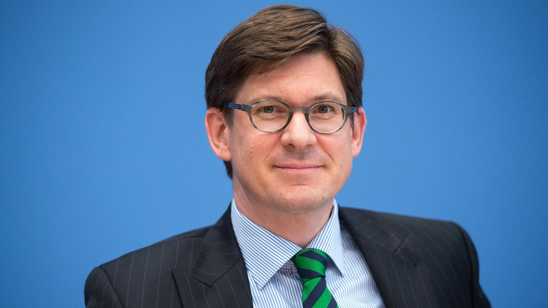 Ole Schröder, Parlamentarischer Staatssekretär im Bundesinnenministerium, in Anzug und mit Brille vor einer blauen Wand sitzend Ole Schröder, Parlamentarischer Staatssekretär im Bundesinnenministerium, in Anzug und mit Brille vor einer blauen Wand sitzend
