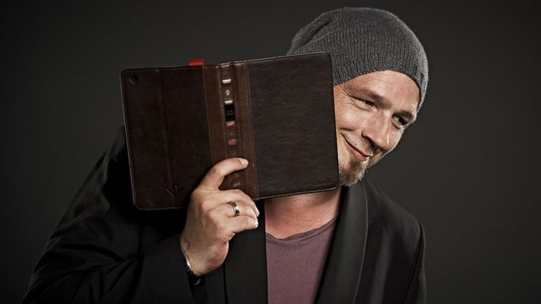 Torsten Sträter hält ein aufgeschlagenes Buch vor dem Gesicht. Torsten Sträter hält ein aufgeschlagenes Buch vor dem Gesicht.