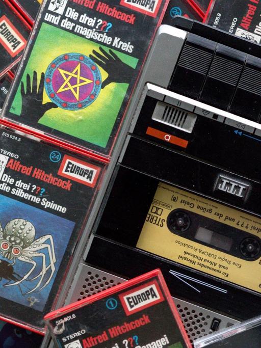 Zahlreiche Kassetten der Hörspielserie "Die drei Fragezeichen" liegen neben einem Kassettenrekorder.