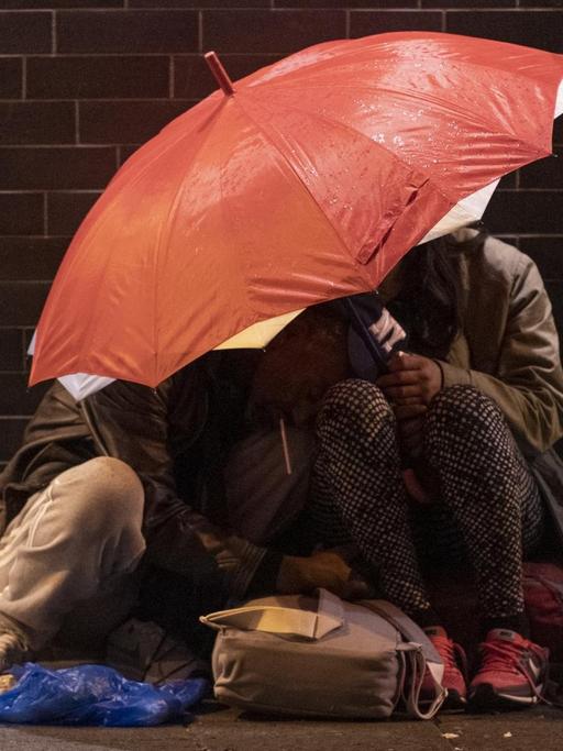 Zwei Menschen haben sich am Rande der Veranstaltung "Bahnhofsviertelnacht" in Frankfurt am Main unter einen Regenschirm zurückgezogen.