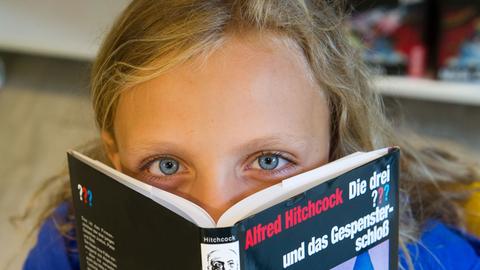 Ein Kind mit einem Buch aus der Reihe "Die drei ???"