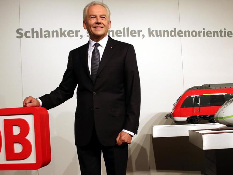 Bahnchef Rüdiger Grube posiert zu Beginn der Halbjahres-Pk für die Fotografen. Er hält die Hand auf ein Bahn-Logo. Neben ihm sind zwei große Modellbahnen zu sehen.