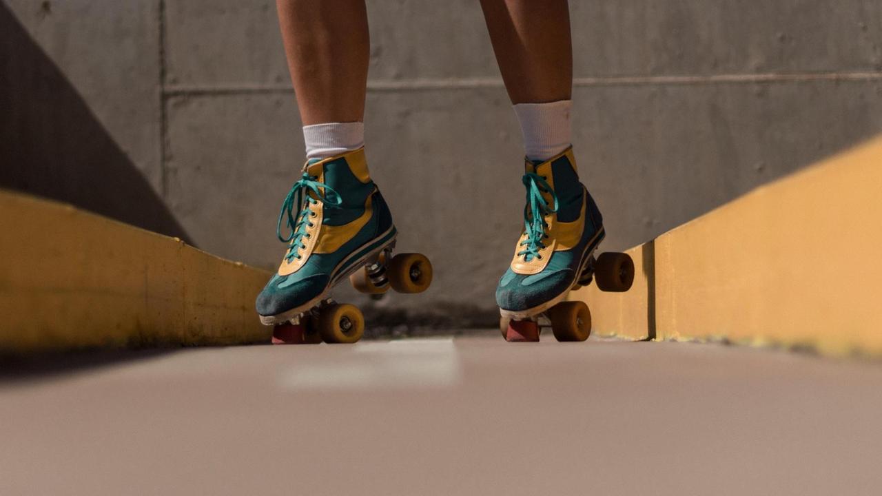 Füße einer Rollschuhläuferin beim Skaten auf Asphalt. Die grün-gelben Rollschuhe haben einen Retrolook und erinern optisch an Turnschuhe.