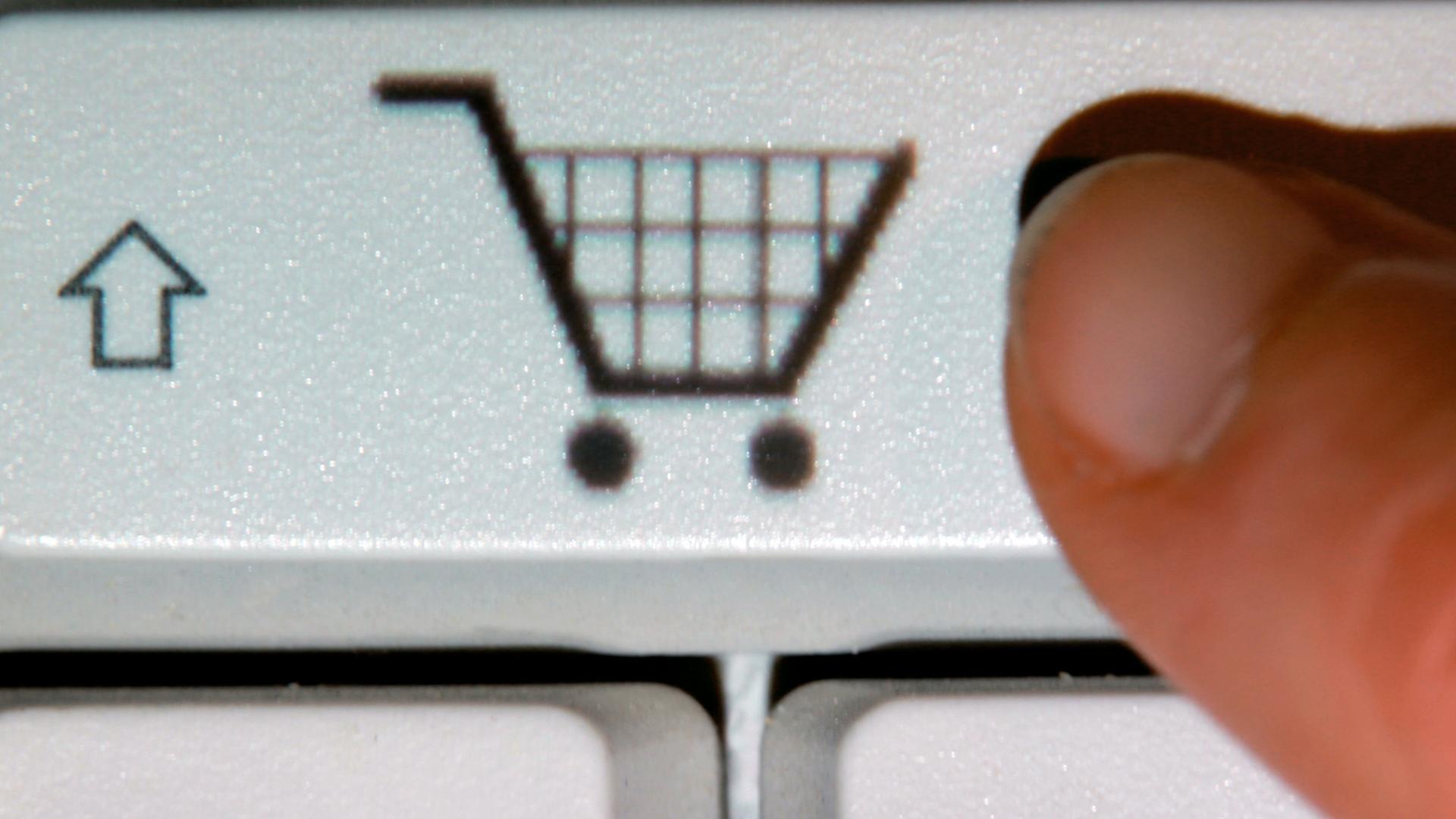 Ein Finger zeigt auf das Symbol eines Einkaufwagens auf einer Taste einer Computertastatur. Ein Finger zeigt auf das Symbol eines Einkaufwagens auf einer Taste einer Computertastatur.