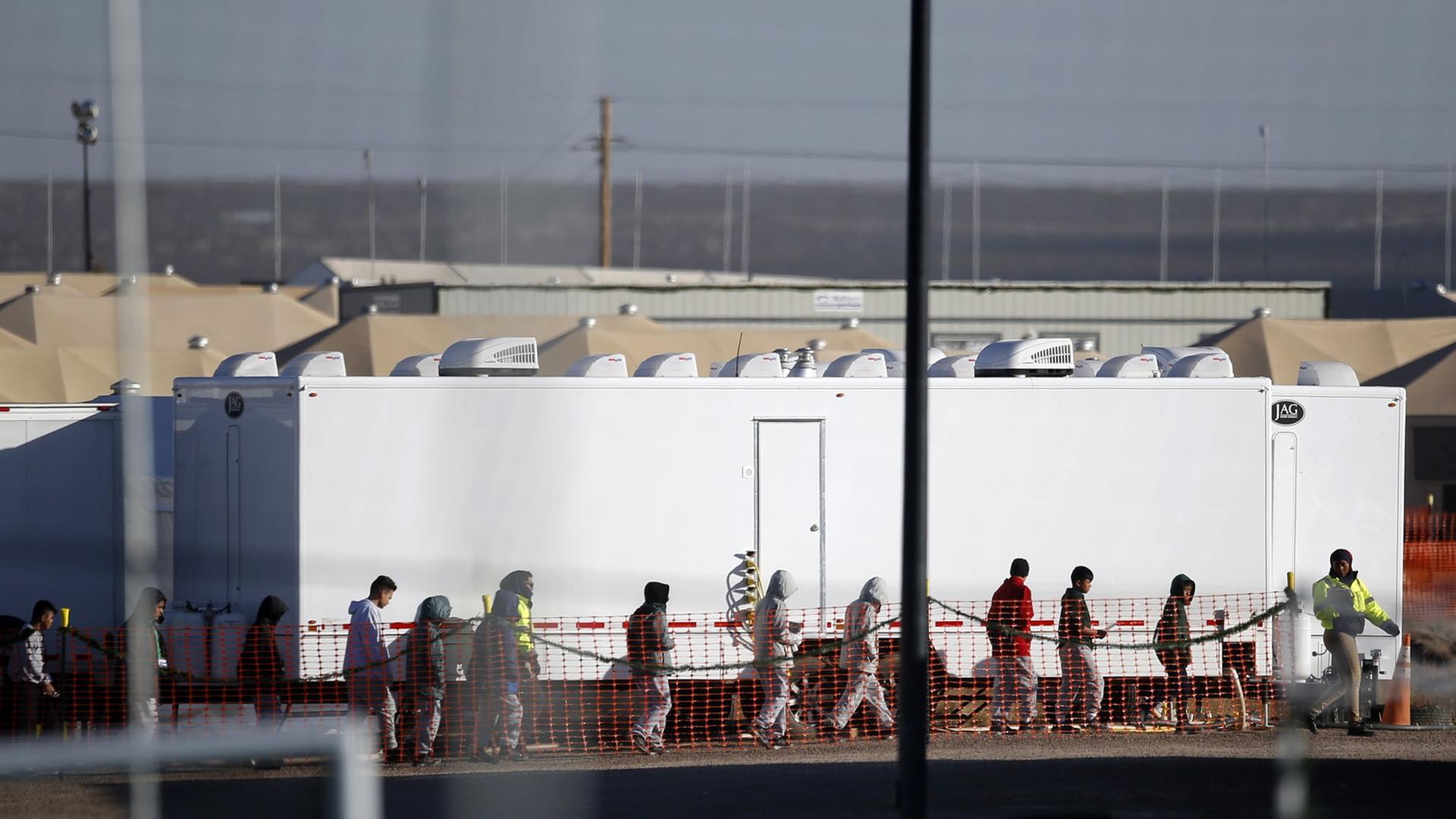 Jugendliche Migranten im Internierungslager in Tornillo, Texas, im Dezember 2018. Hinter einem Zaun laufen, begleitet von Wachpersonal, mehrere junge Menschen. Jugendliche Migranten im Internierungslager in Tornillo, Texas, im Dezember 2018. Hinter einem Zaun laufen, begleitet von Wachpersonal, mehrere junge Menschen.