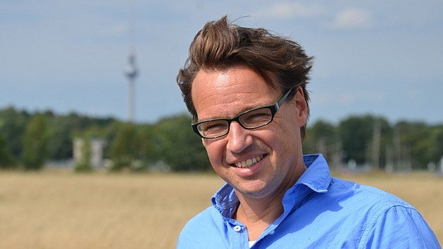 Ein Mann mit blauem Hemd steht auf einer Wiese, die den Blick auf den Berliner Fernsehturm freigibt.