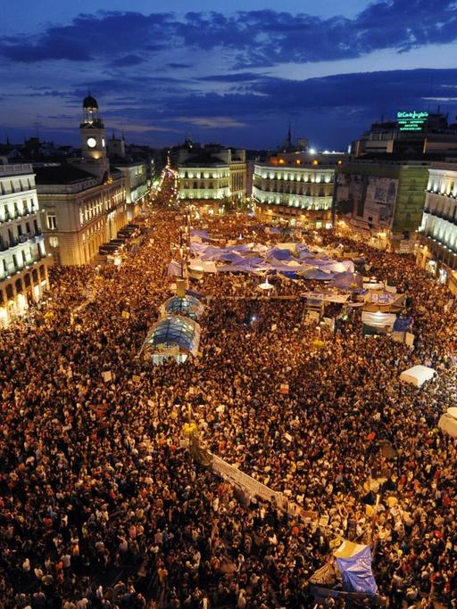 Luftaufnahme vom zentralen Platz Puerta del Sol in Madrid mit Zehntausenden Demonstranten während der Dämmerung.