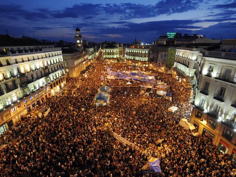 Luftaufnahme vom zentralen Platz Puerta del Sol in Madrid mit Zehntausenden Demonstranten während der Dämmerung.