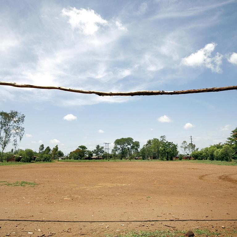 Der Fußballplatz eines Dorfes ohne nennenswerten Rasen und mit einem roh gezimmerten Tor ohne Netz aus Baumstämmen, aufgenommen am 2006 nahe der Stadt Blantyre (Provinz Mphuka) in Malawi.