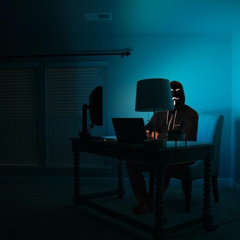 Ein Mann mit Kapuze und Guy Fawkes- Maske sitzt vor einem Computer 