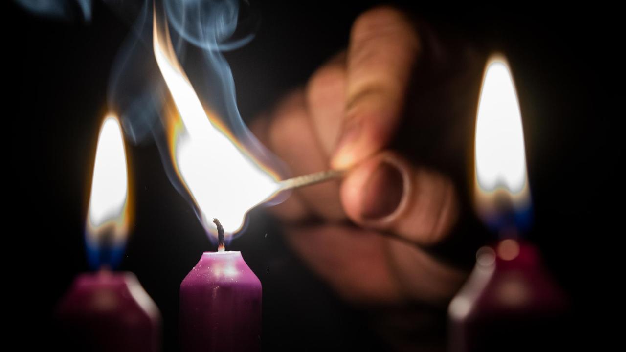 Eine Hand zündet eine Kerze an. Eine Hand zündet eine Kerze an.