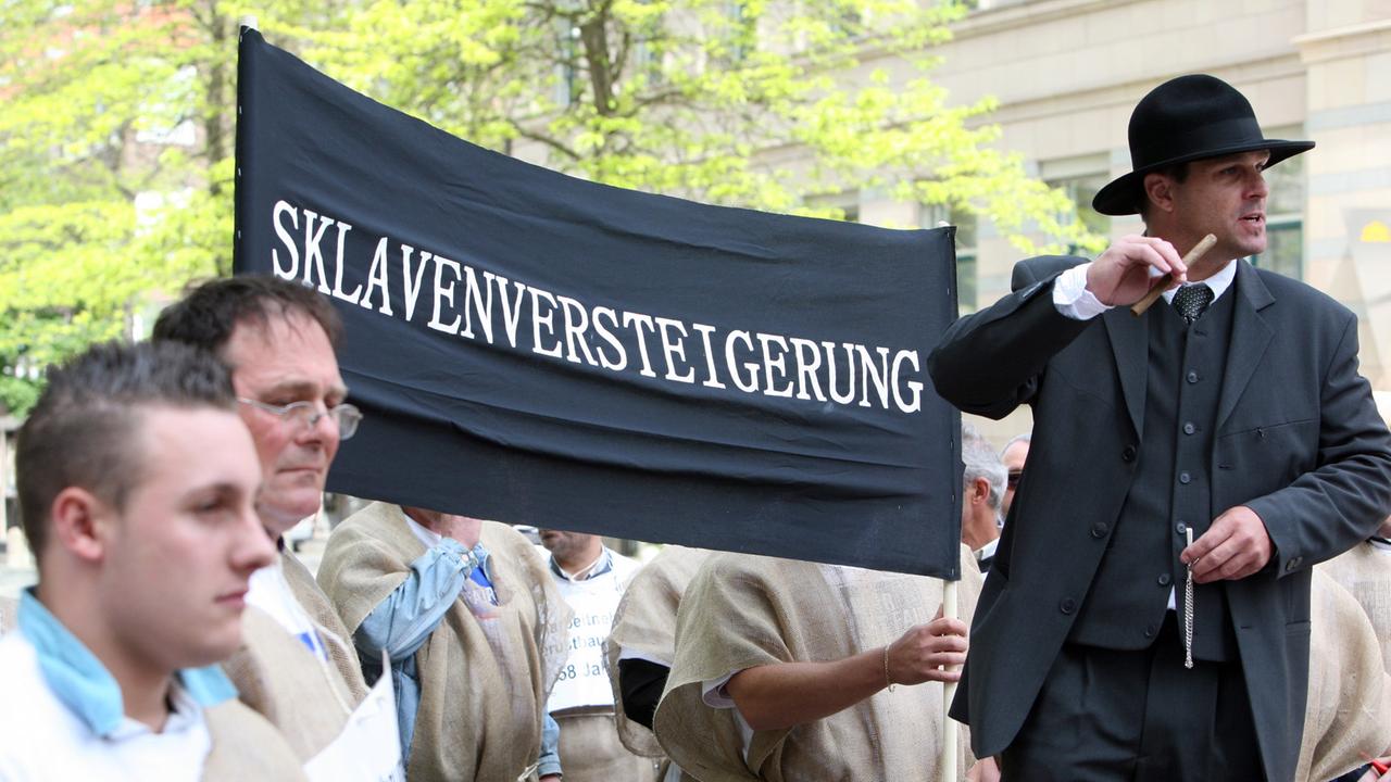 Als Sklaven verkleidete Gerüstbauer werden in Kiel symbolisch als "Arbeitssklaven" versteigert. Als Sklaven verkleidete Gerüstbauer werden in Kiel symbolisch als "Arbeitssklaven" versteigert.