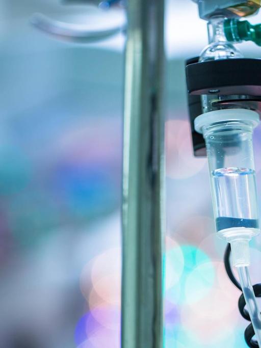 Ein Tropf hängt in einem Operationssaal in einem Krankenhaus, im Hintergrund verschwommene Lichter.