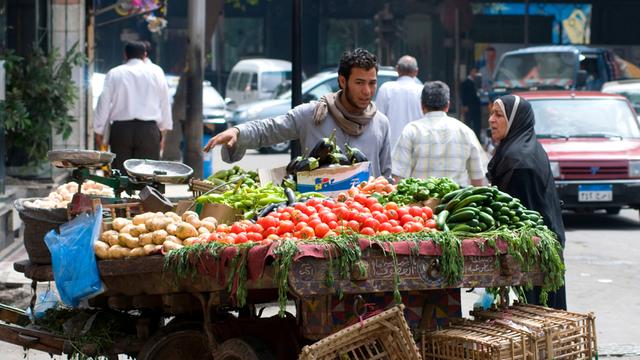 Eine Frau unterhält sich mit einem Gemüsehändler an dessen fahrbaren Stand auf einer Straße in der Innenstadt von Kairo.