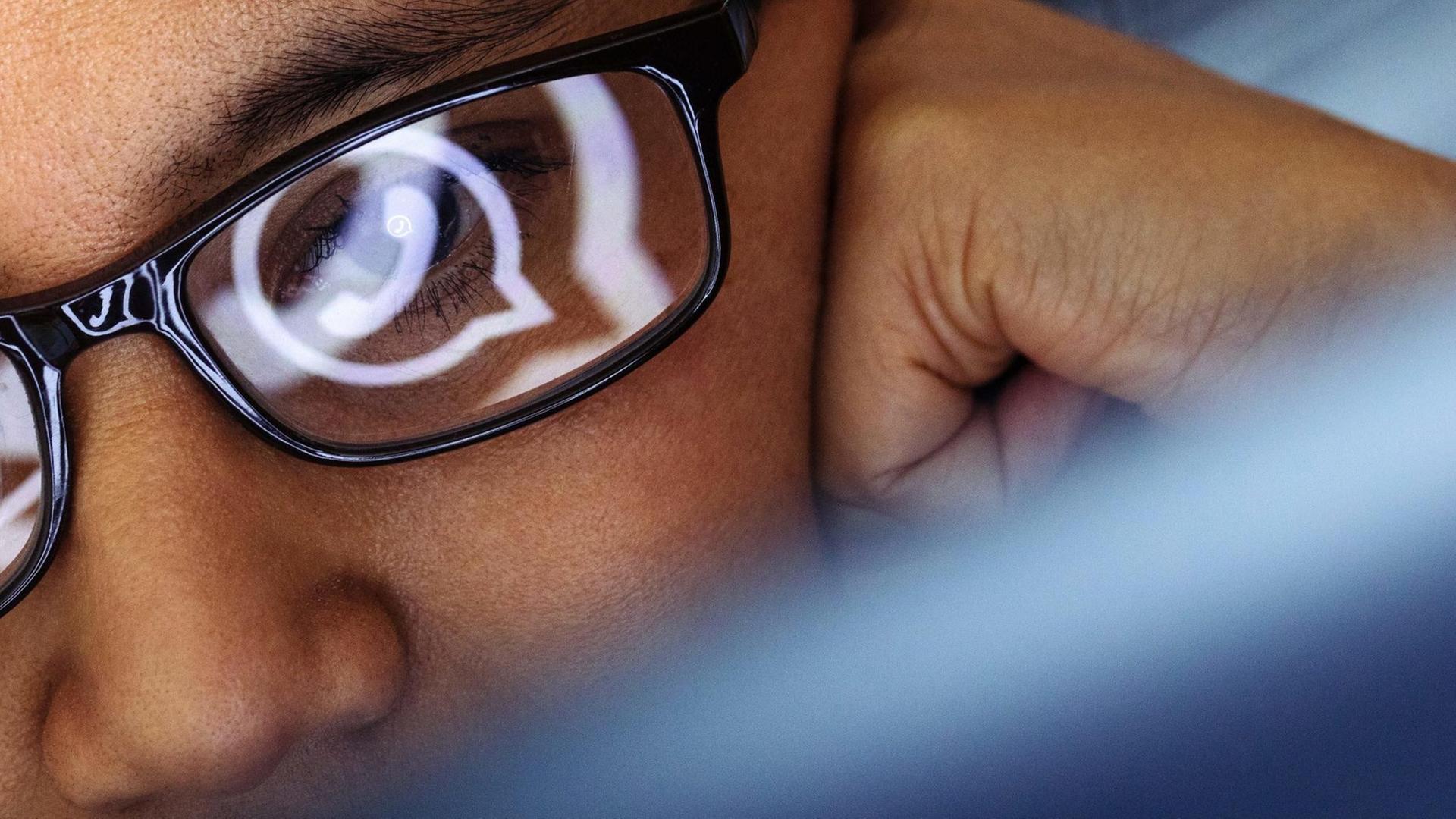 Eine Laptop-Benutzerin mit dunklem Brillengestell blickt auf ein WhatsApp-Symbol.