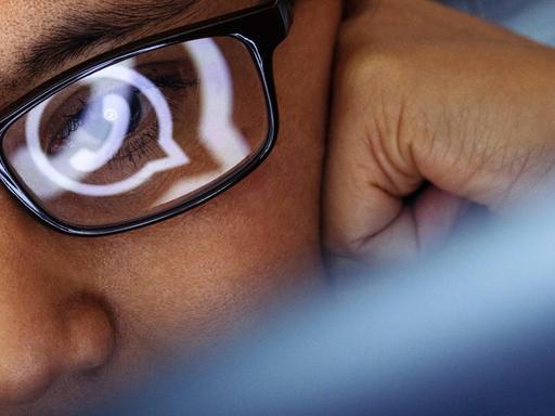 Eine Laptop-Benutzerin mit dunklem Brillengestell blickt auf ein WhatsApp-Symbol.