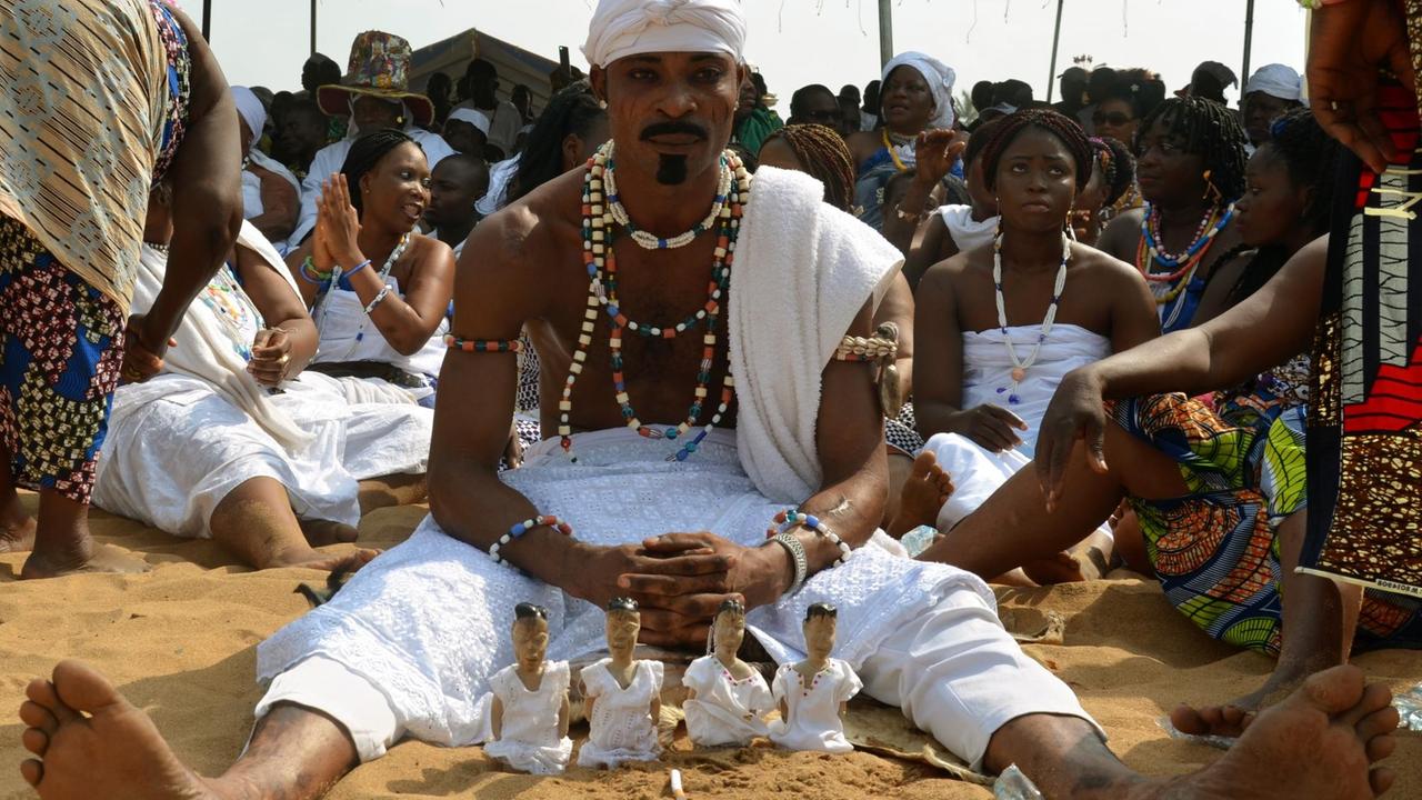 Ein Mann sitzt am Strand von Benin mit Holzpüppchen. Diese symbolisieren, dass ein Zwilling verloren wurde und erinnern daran. Ein Mann sitzt am Strand von Benin mit Holzpüppchen. Diese symbolisieren, dass ein Zwilling verloren wurde und erinnern daran.