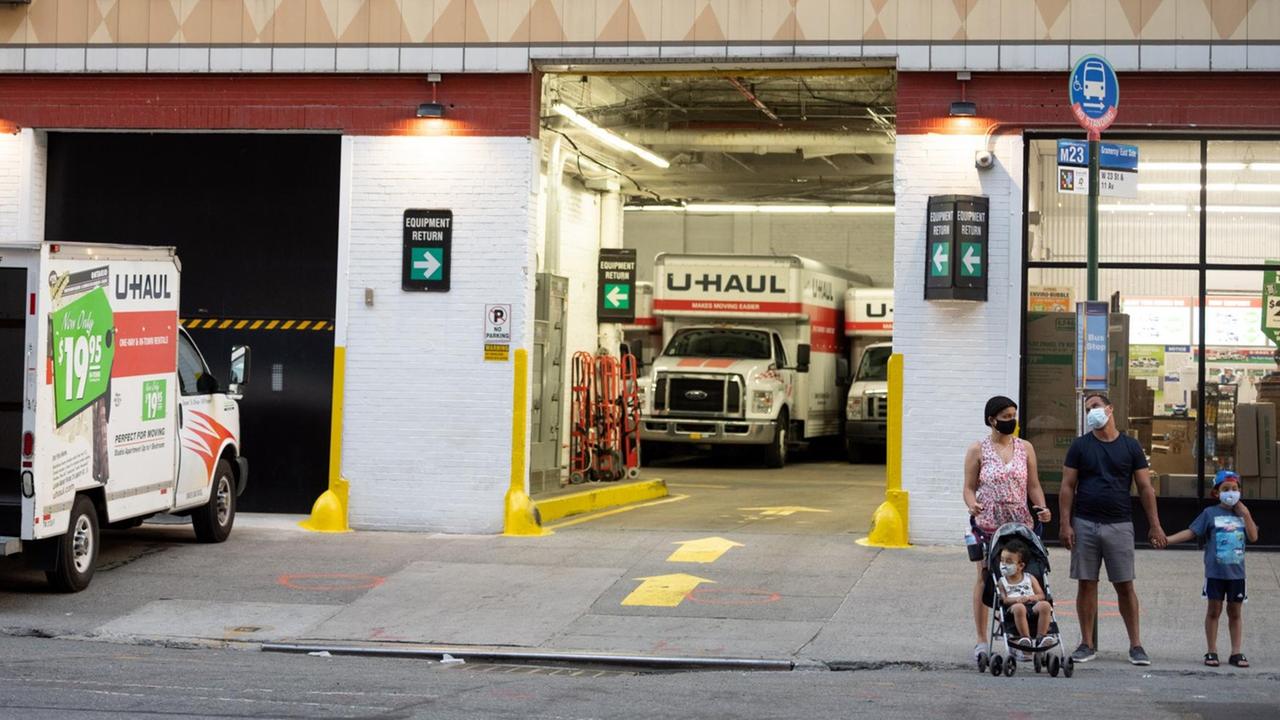 Eine Familie, mit Mund- und Nasenschutz, steht auf dem Bürgersteig, vor der Filiale einer Firma, die LKWs für Umzüge und Transporte in New York City vermietet. Eine Familie, mit Mund- und Nasenschutz, steht auf dem Bürgersteig, vor der Filiale einer Firma, die LKWs für Umzüge und Transporte in New York City vermietet.