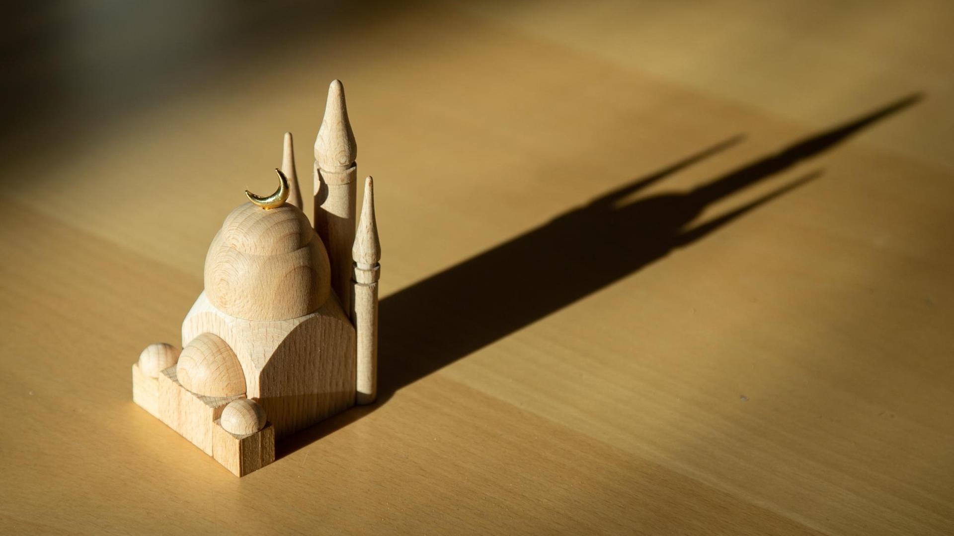 Eine kleine Holz-Moschee auf einem Tisch wirft lange Schatten. Eine kleine Holz-Moschee auf einem Tisch wirft lange Schatten.