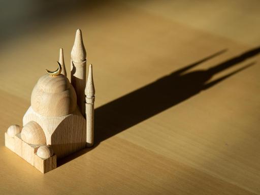 Eine kleine Holz-Moschee auf einem Tisch wirft lange Schatten.