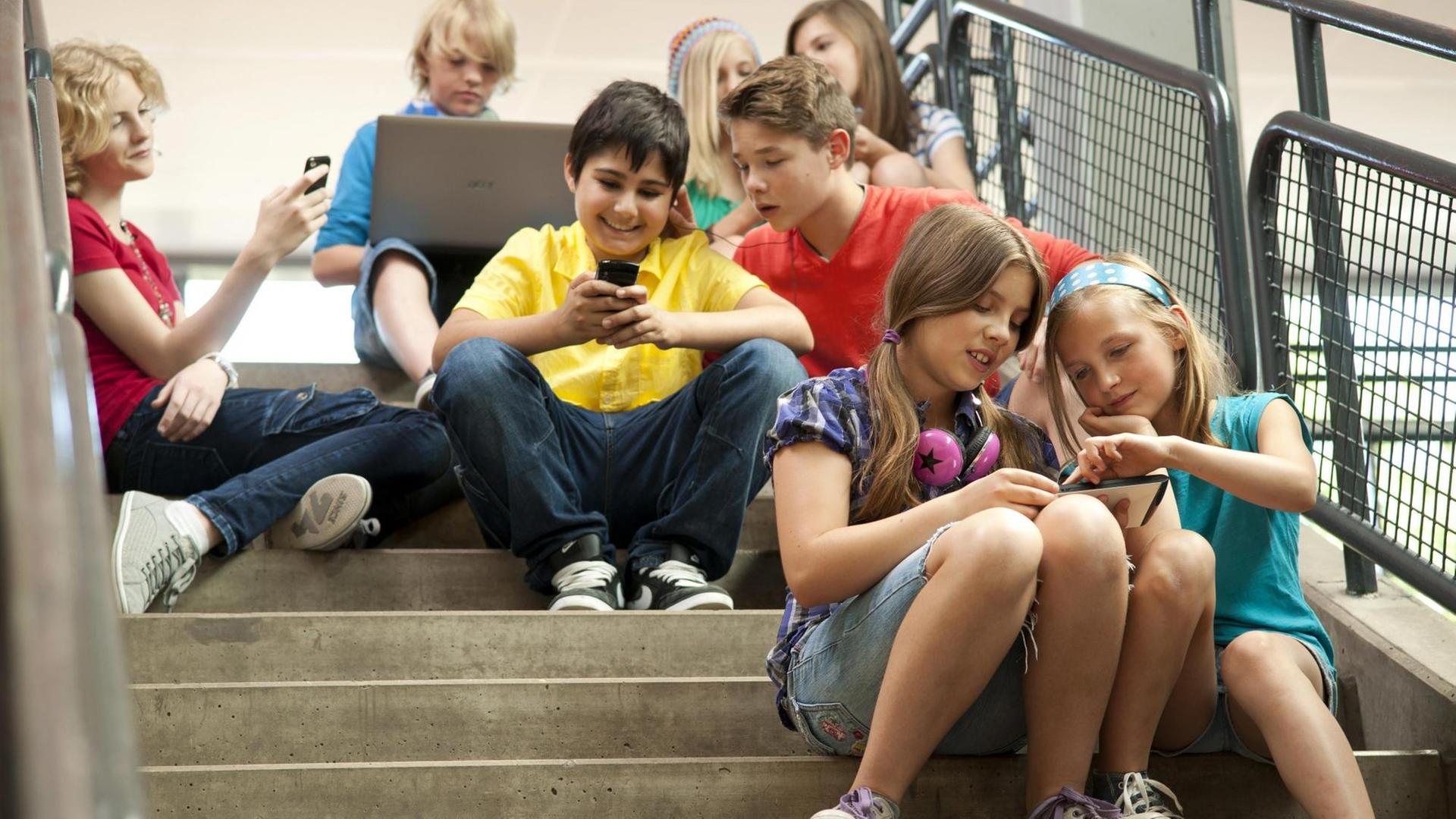 Gruppe Schüler sitzt auf einer Treppe und schaut auf Tablet-PCs und Smartphones