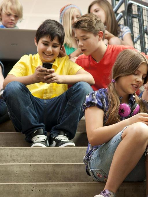 Gruppe Schüler sitzt auf einer Treppe und kommuniziert mit Tablet-PCs und Smartphones | Verwendung weltweit, Keine Weitergabe an Wiederverkäufer. | dpa / picture alliance / imageBROKER