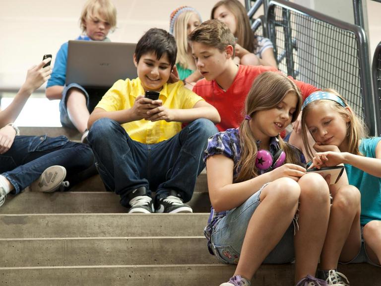 Gruppe Schüler sitzt auf einer Treppe und kommuniziert mit Tablet-PCs und Smartphones | Verwendung weltweit, Keine Weitergabe an Wiederverkäufer. | dpa / picture alliance / imageBROKER