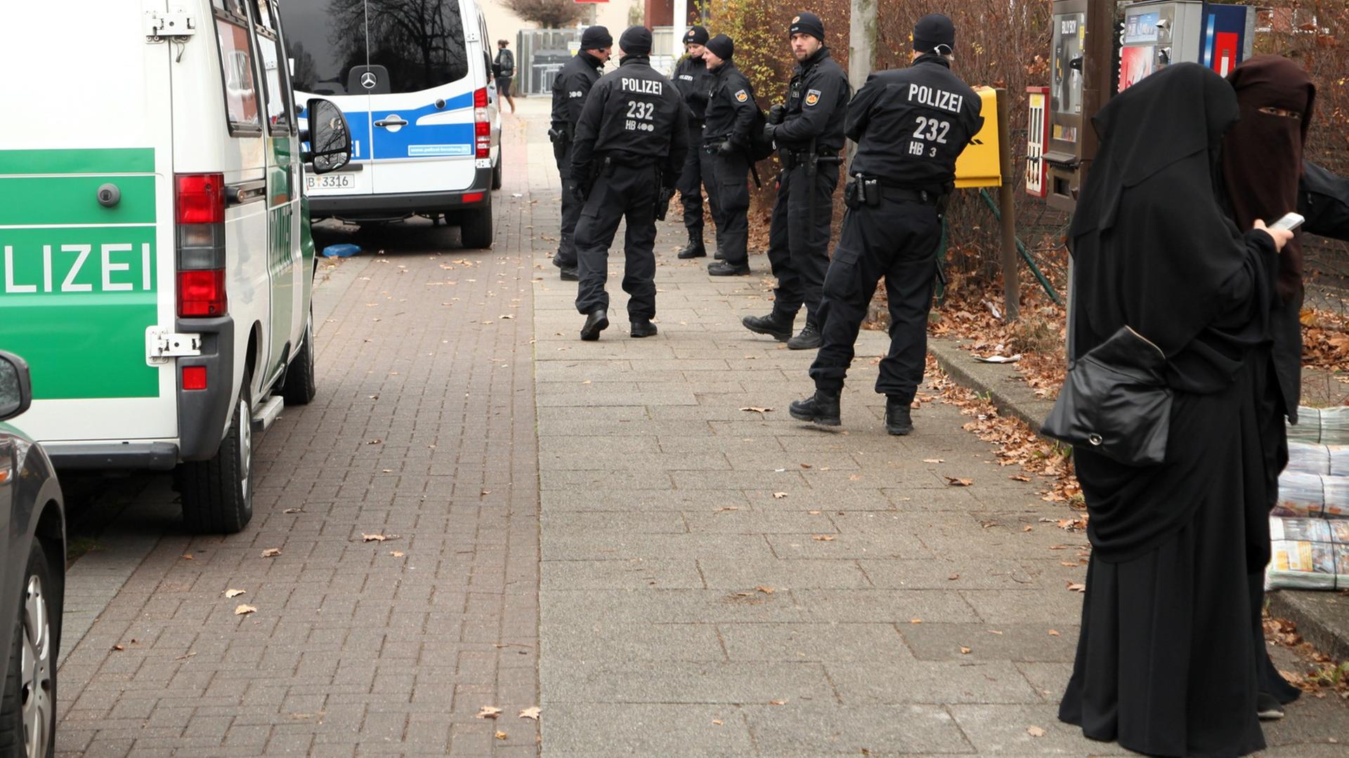Polizeiwagen und Beamte stehen in Bremen während einer Durchsuchung vor dem salafistischen Kultur & Familien Verein (KuF) im Stadtteil Gröpelingen neben zwei Frauen, die vollkommen verschleiert sind. Polizeiwagen und Beamte stehen in Bremen während einer Durchsuchung vor dem salafistischen Kultur & Familien Verein (KuF) im Stadtteil Gröpelingen neben zwei Frauen, die vollkommen verschleiert sind.