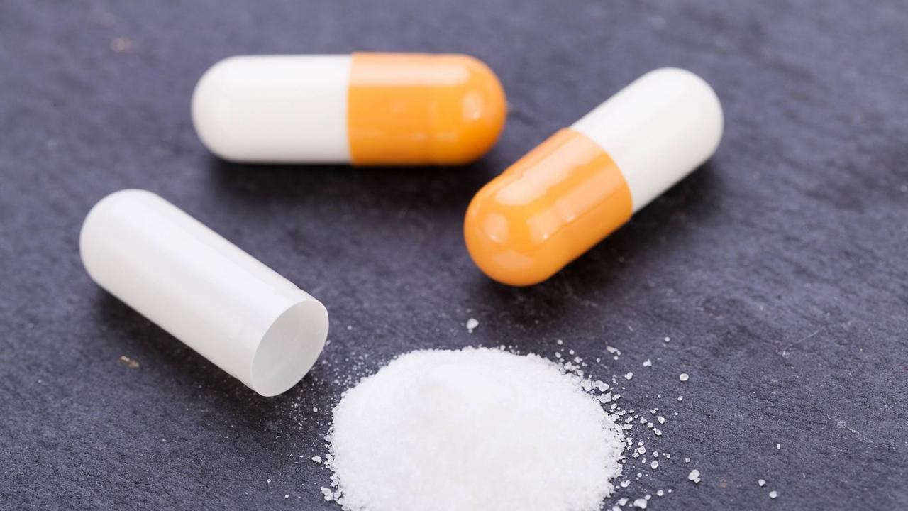 Weiß-orangefarbene Pillen und weißes Pulver auf schwarzem Hintergrund. Weiß-orangefarbene Pillen und weißes Pulver auf schwarzem Hintergrund.