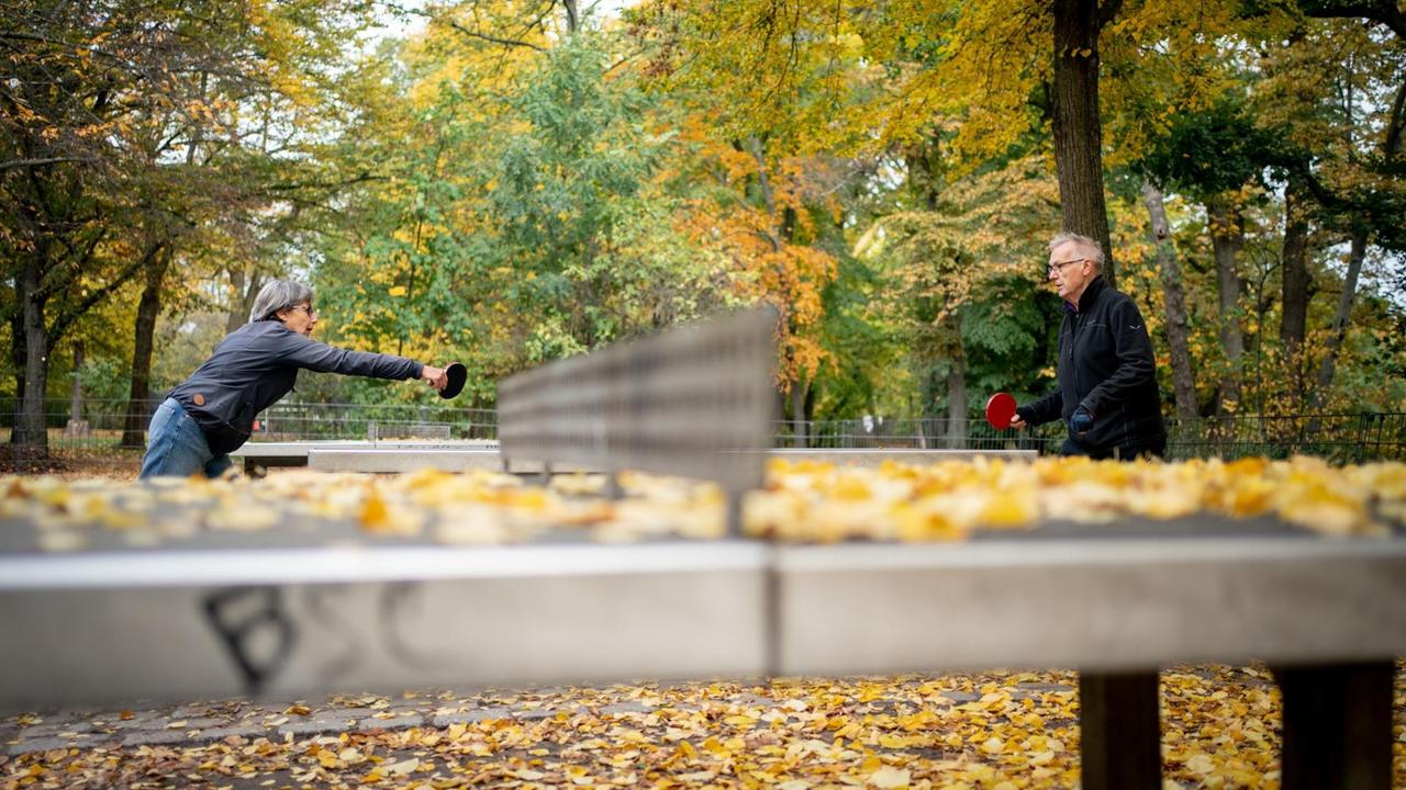 Besucher des Volksparks Wilmersdorf spielen zwischen heruntergefallenem Herbstlaub und bunt gefärbten Bäumen Tischtennis. Besucher des Volksparks Wilmersdorf spielen zwischen heruntergefallenem Herbstlaub und bunt gefärbten Bäumen Tischtennis.